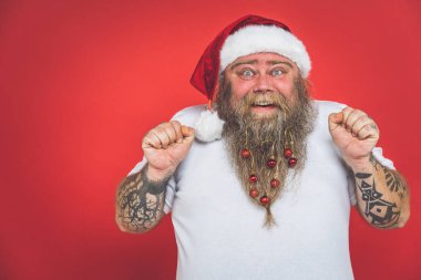 Dövmeli komik çılgın noel baba kırmızı renkli arka planda eğleniyor.
