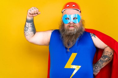 Süper kahraman kostümlü komik şişman adam özel güçleri olan süper insan rolünde, renkli arka planda bir portre.