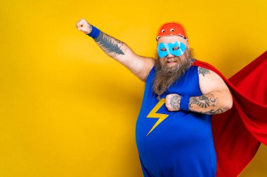 Süper kahraman kostümlü komik şişman adam özel güçleri olan süper insan rolünde, renkli arka planda bir portre.