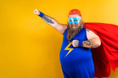 Süper kahraman kostümlü komik şişman adam özel güçleri olan süper insan rolünde, renkli arka planda bir portre.