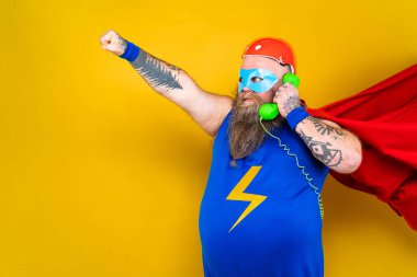 Süper kahraman kostümlü komik şişman adam özel güçleri olan süper insan rolünde, renkli arka planda bir portre.