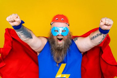 Süper kahraman kostümlü komik şişman adam özel güçleri olan süper insan rolünde, renkli arka planda bir portre.
