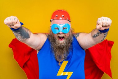 Süper kahraman kostümlü komik şişman adam özel güçleri olan süper insan rolünde, renkli arka planda bir portre.