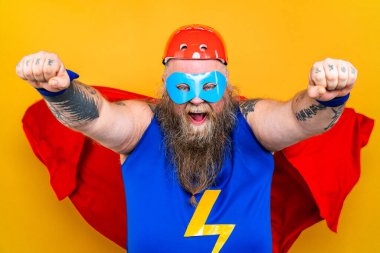 Süper kahraman kostümlü komik şişman adam özel güçleri olan süper insan rolünde, renkli arka planda bir portre.