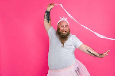 Balerin gibi davranan komik şişman adam, pembe arka planda dans eden sakallı ve dövmeli komik bir karakter.