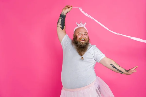 Funny fat man pretending to be a ballerina with tutu - Comic character with beard and tattooes dancing on a pink background