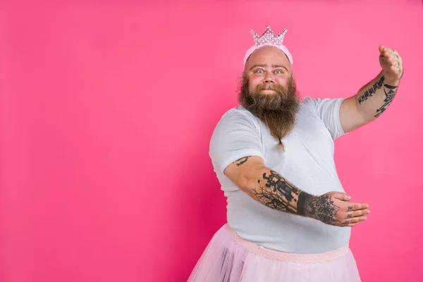 Funny fat man pretending to be a ballerina with tutu - Comic character with beard and tattooes dancing on a pink background
