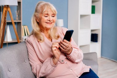 Güzel, son sınıf öğrencisi bir kadın evde tek başına oturuyor ve internete bağlanmak için akıllı telefon cihazı kullanıyor.