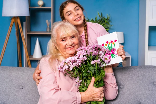 Grandchild presenting flowers to granny at home, happy domestic life moments - Family having fun, concepts about elderly, mult-generation family and relationship