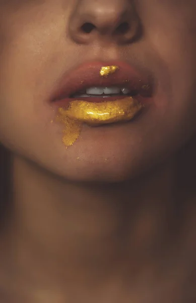 Artistic image of a female mouth with golden fluid dripping on the chin