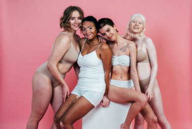 Farklı tür ten rengine sahip çok ırklı bir grup kadın stüdyoda birlikte poz veriyor. Vücut pozitifliği ve kendini kabullenme kavramı