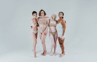 Farklı tür ten rengine sahip çok ırklı bir grup kadın stüdyoda birlikte poz veriyor. Vücut pozitifliği ve kendini kabullenme kavramı