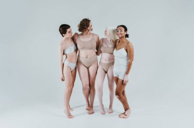 Farklı tür ten rengine sahip çok ırklı bir grup kadın stüdyoda birlikte poz veriyor. Vücut pozitifliği ve kendini kabullenme kavramı