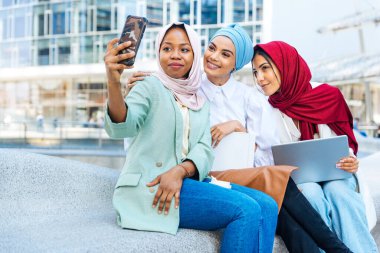 Çok ırklı Müslüman kızlar günlük kıyafetler giyip, geleneksel tesettüre girip dışarıda eğleniyorlar. 3 Arap genç kız.