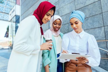 Çok ırklı Müslüman kızlar günlük kıyafetler giyip, geleneksel tesettüre girip dışarıda eğleniyorlar. 3 Arap genç kız.