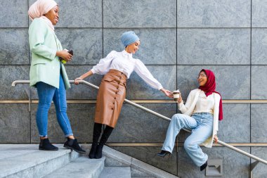Çok ırklı Müslüman kızlar günlük kıyafetler giyip, geleneksel tesettüre girip dışarıda eğleniyorlar. 3 Arap genç kız.