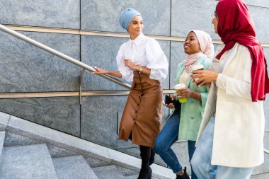 Çok ırklı Müslüman kızlar günlük kıyafetler giyip, geleneksel tesettüre girip dışarıda eğleniyorlar. 3 Arap genç kız.