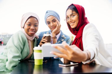 Çok ırklı Müslüman kızlar günlük kıyafetler giyip, geleneksel tesettüre girip dışarıda eğleniyorlar. 3 Arap genç kız.