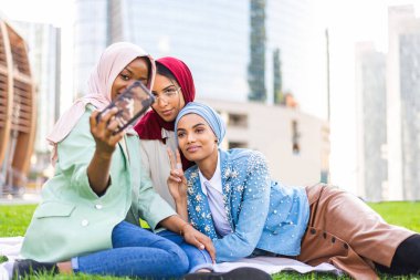 Çok ırklı Müslüman kızlar günlük kıyafetler giyip, geleneksel tesettüre girip dışarıda eğleniyorlar. 3 Arap genç kız.