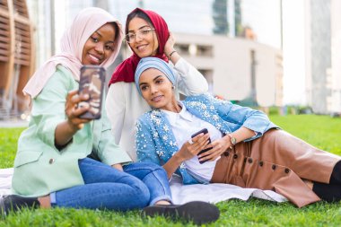 Çok ırklı Müslüman kızlar günlük kıyafetler giyip, geleneksel tesettüre girip dışarıda eğleniyorlar. 3 Arap genç kız.