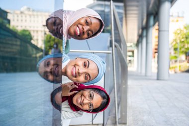 Çok ırklı Müslüman kızlar günlük kıyafetler giyip, geleneksel tesettüre girip dışarıda eğleniyorlar. 3 Arap genç kız.