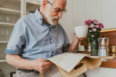 Yaşlı adam evde dinleniyor, gazete okuyor ve kahvaltı yapıyor.