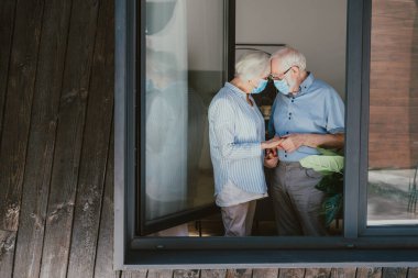Covid-19 pandemik karantina sırasında evde koruyucu maskeli yaşlı bir çift - Karantina altındaki yaşlılar sosyal mesafeye ve koronavirüs virüsüne karşı izolasyon yayıldı