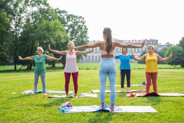 Parkta fitness eğitmeniyle eğitim gören çok ırklı yaşlı kadınlar grubu - aktif yaşlılar spor yapıyor.