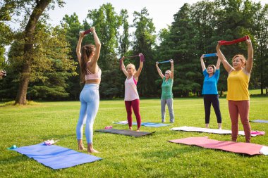 Parkta fitness eğitmeniyle eğitim gören çok ırklı yaşlı kadınlar grubu - aktif yaşlılar spor yapıyor.