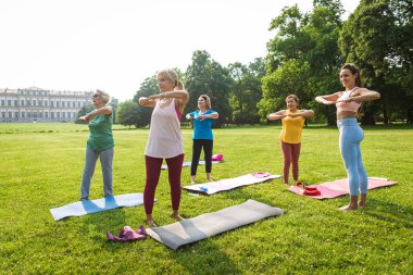 Parkta fitness eğitmeniyle eğitim gören çok ırklı yaşlı kadınlar grubu - aktif yaşlılar spor yapıyor.