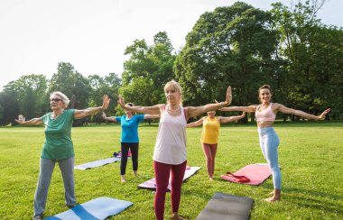 Parkta fitness eğitmeniyle eğitim gören çok ırklı yaşlı kadınlar grubu - aktif yaşlılar spor yapıyor.