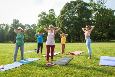 Parkta fitness eğitmeniyle eğitim gören çok ırklı yaşlı kadınlar grubu - aktif yaşlılar spor yapıyor.