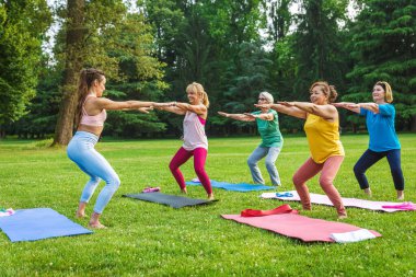 Parkta fitness eğitmeniyle eğitim gören çok ırklı yaşlı kadınlar grubu - aktif yaşlılar spor yapıyor.