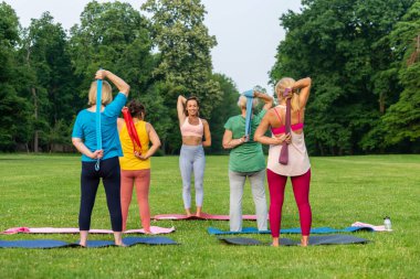Parkta fitness eğitmeniyle eğitim gören çok ırklı yaşlı kadınlar grubu - aktif yaşlılar spor yapıyor.