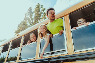 İlkokula giden bir grup genç öğrenci sarı okul otobüsüyle, ilkokul çocukları eğleniyor.