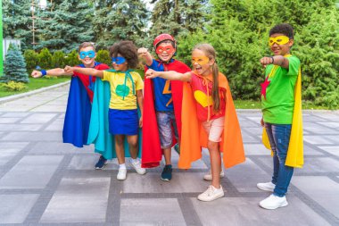 Multiracial group of young schooler wearing superhero costumes and having fun outdoors clipart