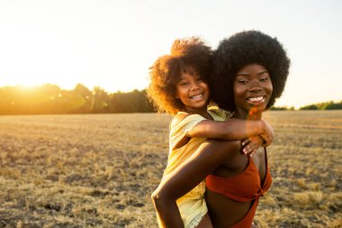 Güzel Afro-Amerikan anne ve kızı ayçiçeği tarlasında eğleniyor ve eğleniyorlar.