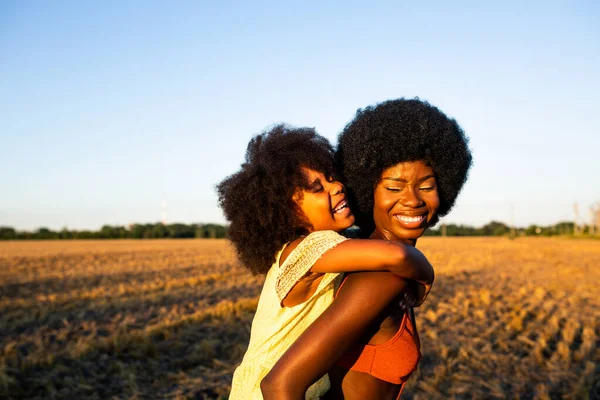美しいアフロ系アメリカ人のお母さんと娘がひまわり畑で遊んで楽しんでいます — ストック写真