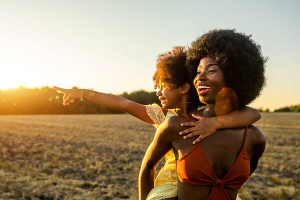 Beautiful afro-american mom and daughter palying and having fun in a sunflowers field