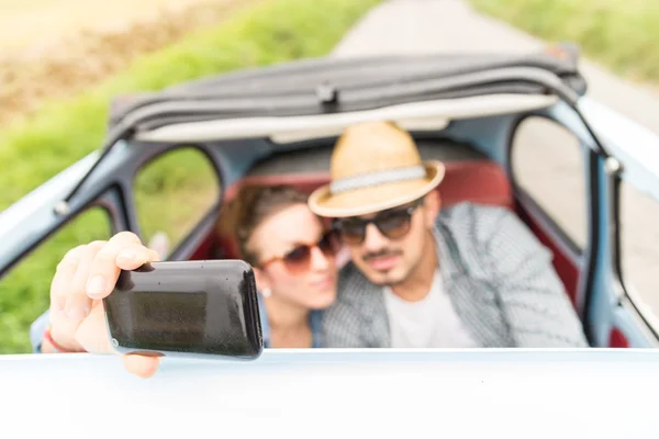 Pareja feliz tomando una selfie en un coche vintage — Foto de Stock