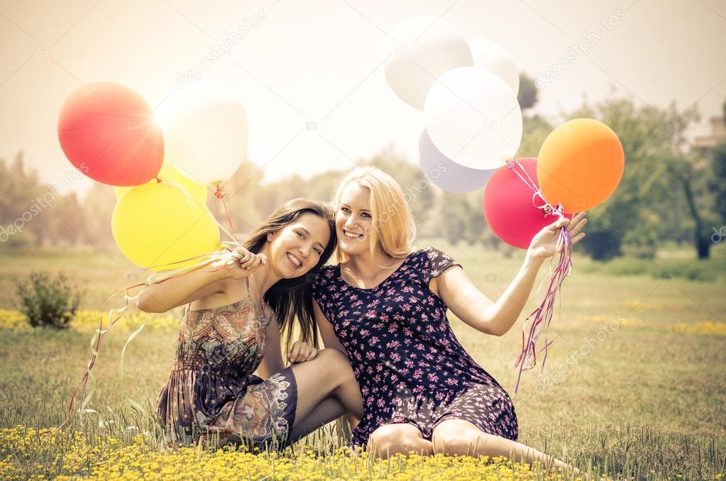 couple of girls sitting in the park with balloons 