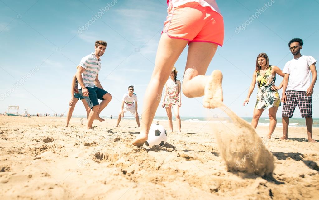 group of friends playing soccer on the beach 