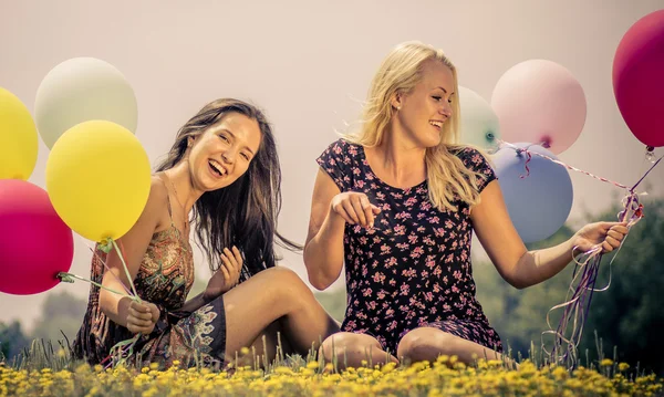 Två flickor liggande i gräset med ballonger — Stockfoto