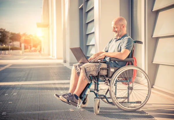 Человек на инвалидной коляске с помощью компьютера — стоковое фото