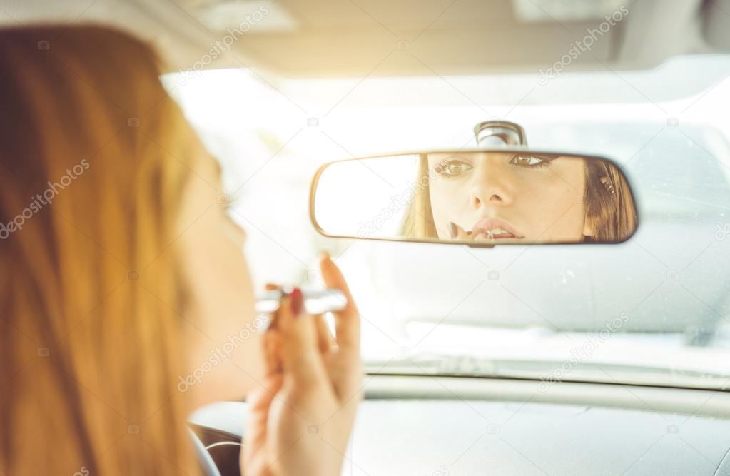 woman putting lipstick in the car.