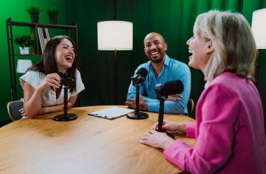 Üç farklı yetişkin sunucu, bir adam ve iki kadın, mikrofonlu bir masanın etrafında oturmuş, canlı bir podcast tartışmasına girişiyor ya da perdeli bir stüdyo ortamında röportaj yapıyorlar.