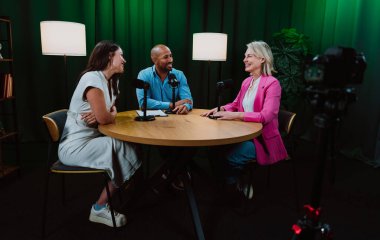 Üç farklı yetişkin sunucu, bir adam ve iki kadın, mikrofonlu bir masanın etrafında oturmuş, canlı bir podcast tartışmasına girişiyor ya da perdeli bir stüdyo ortamında röportaj yapıyorlar.