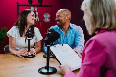 Üç farklı birey, bir ev sahibi ve birkaç konuk, bir ses podcast 'i kaydederken gülümsüyor ve sohbete dalıyorlar ya da profesyonel bir stüdyoda mikrofonla canlı yayın yapıyorlar.