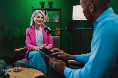 Profesyonel bir podcast stüdyosunda, mikrofonlar ve kameralarla yayın yapan, dinamik bir konuşma yapan üç kişiden oluşan bir grup.