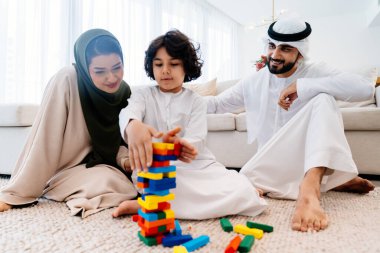Geleneksel emirati kıyafetleri giyen Ortadoğu ailesi evde birlikte vakit geçiriyorlar. Arap ebeveynler ve oğulları oturma odasında oyun oynuyorlar.